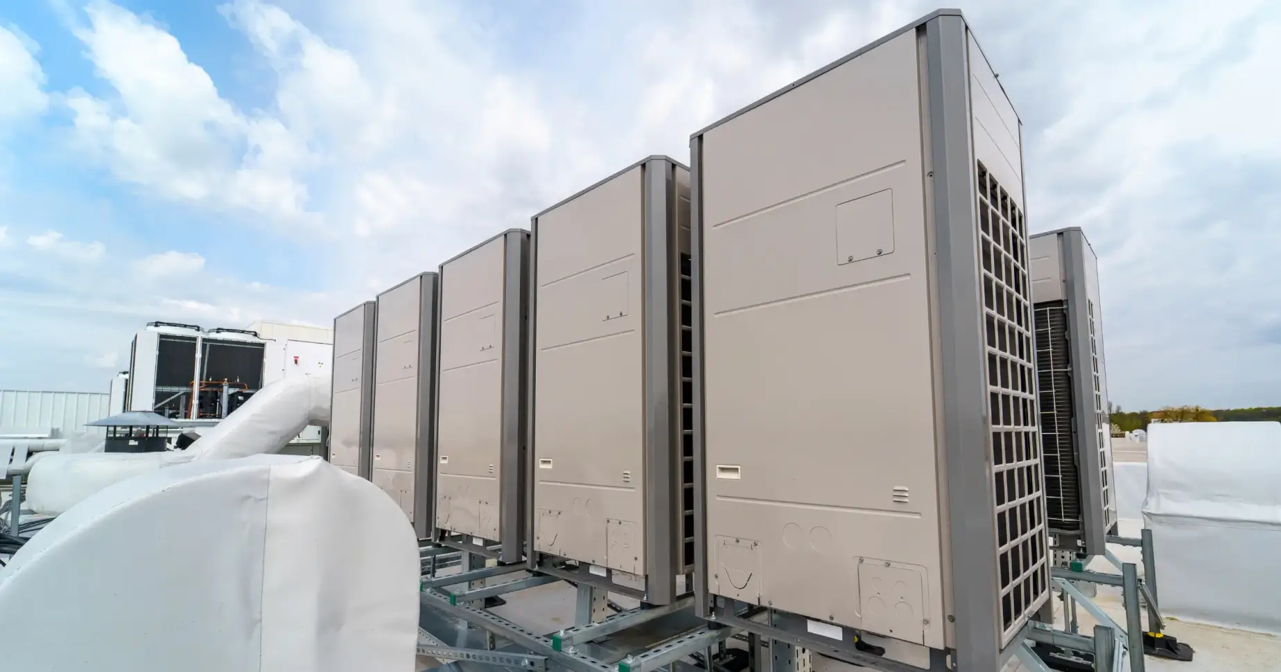 Row of large rooftop HVAC units/chillers mounted on a metal frame against a blue sky.